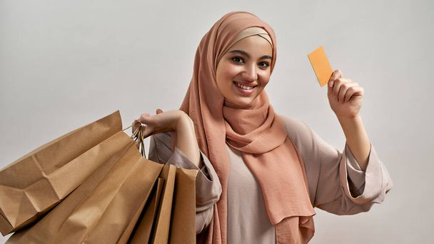 Smiling arabian girl in hijab with bags and card - Zdjęcie, obraz