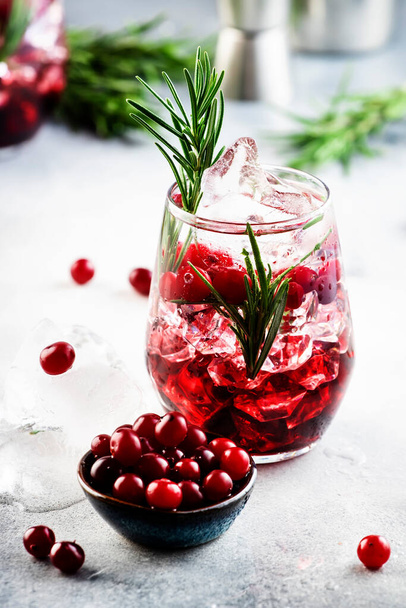 Cranberry, vodka, gin alcoholic cocktail with ice, rosemary and berries in tumbler glass. Summer long drink. Gray table background - Φωτογραφία, εικόνα