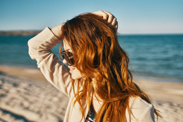 glückliche Reisende am Strand in der Nähe des Meeres rote Haare beige Mantel Sandinsel - Foto, Bild
