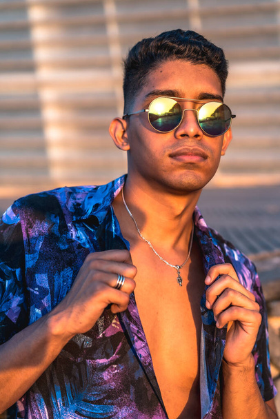 Summer lifestyle, a young Latino enjoying summer vacations. with purple flower shirt and sunglasses, watching the sunset - Foto, imagen