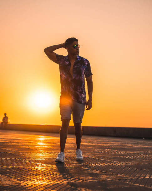 Summer lifestyle, a young Latino enjoying summer vacations. with purple flower shirt and sunglasses, strolling in the sunset - Foto, immagini