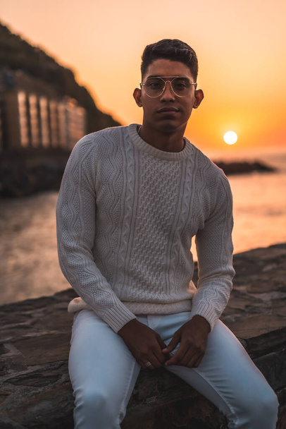 Summer lifestyle, a young Latino enjoying summer vacations. dressed in white with pants and sweater, enjoying the sunset, vertical photo - Photo, Image