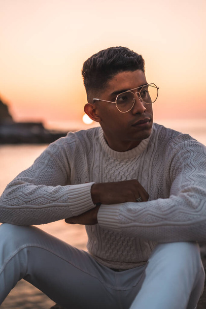 Summer lifestyle, a young Latino enjoying summer vacations. dressed in white with pants and sweater, pensive by the sea - Fotó, kép
