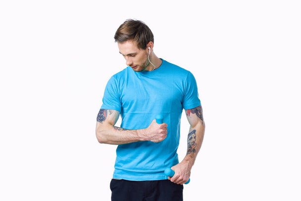 cara com halteres entrar para esportes em uma camiseta azul em um fundo leve - Foto, Imagem