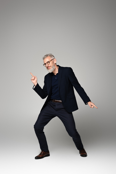 Mann mittleren Alters in Brille und Anzug tanzt auf grau - Foto, Bild