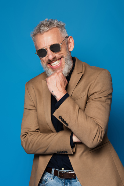 veselý muž středního věku ve slunečních brýlích izolovaných na modré - Fotografie, Obrázek