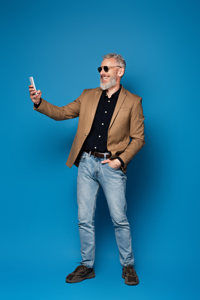 満足のいく中年男性でサングラスをかけますセルフィーオン携帯電話上の青 - 写真・画像
