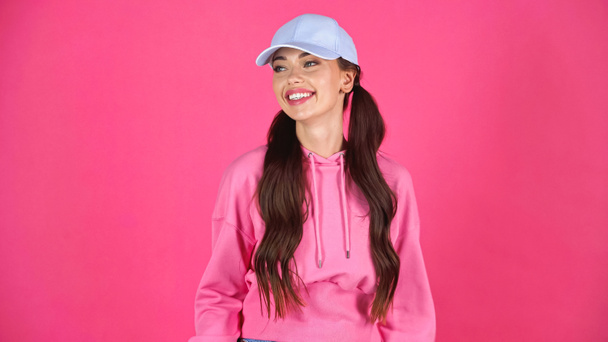улыбающаяся молодая женщина в кепке и толстовке, смотрящая на розовый - Фото, изображение