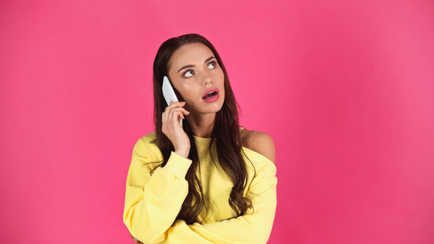 thoughtful young adult woman with open mouth speaking on cellphone isolated on pink  - Foto, Imagen
