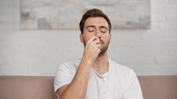 allergic man with closed eyes using nasal spray at home  - Foto, afbeelding
