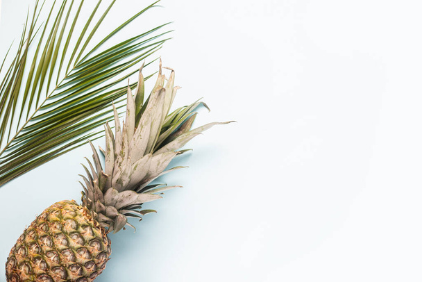 hele rijpe ananas en een blad van een palmboom op een lichte achtergrond. Bovenaanzicht, vlak lay. - Foto, afbeelding