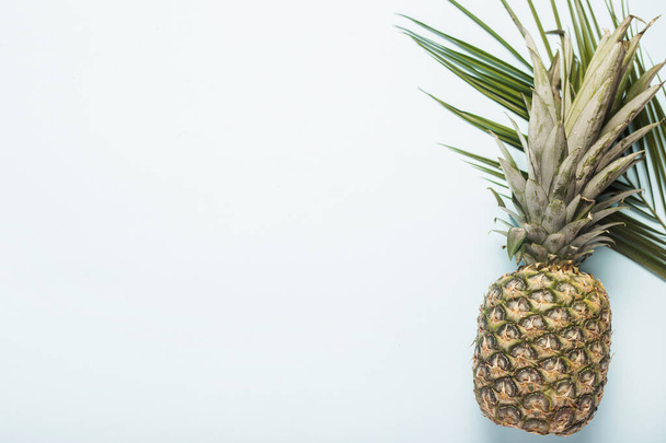 kokonainen kypsä ananas ja vaalealla pohjalla oleva palmun lehti. Top view, tasainen lay. - Valokuva, kuva