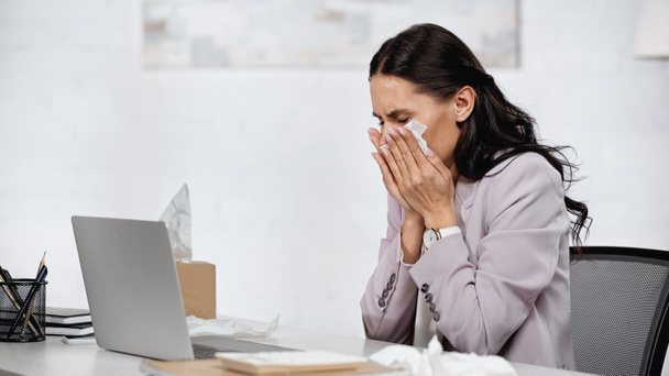 allergic woman sneezing in tissue near laptop on desk in office - Foto, imagen