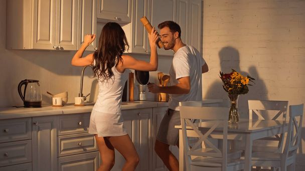 cheerful man with frying pan dancing near girlfriend with paper mill   - Fotó, kép