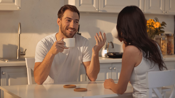 happy man holding cup and talking with blurred brunette girlfriend  - Foto, afbeelding