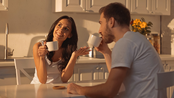 happy young woman holding cup of coffee and talking with blurred boyfriend  - Photo, image