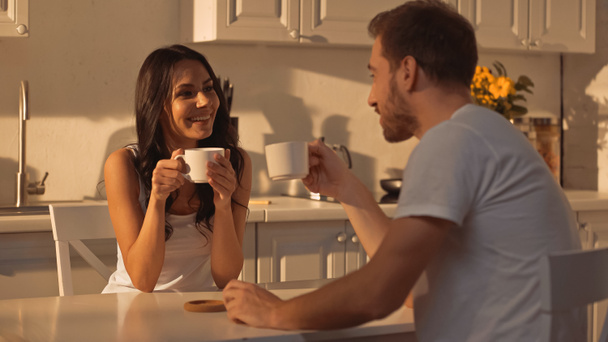 joyful young woman holding cup and smiling near blurred boyfriend  - Zdjęcie, obraz