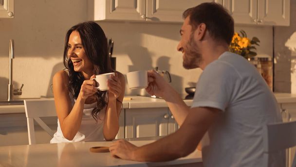 happy young woman holding cup and smiling near blurred boyfriend  - Foto, afbeelding
