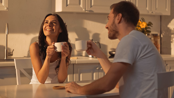 cheerful young woman holding cup and smiling near boyfriend  - Foto, imagen
