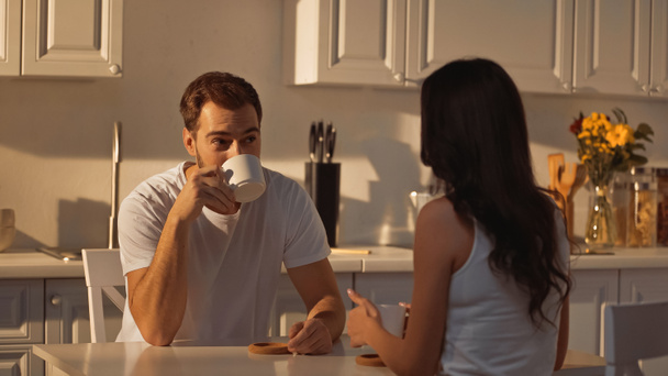 man drinking coffee and looking at brunette girlfriend in kitchen  - Foto, Imagem