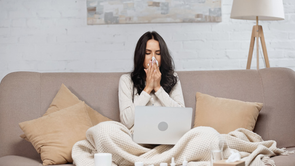 ill woman sneezing in tissue while looking at laptop  - Foto, immagini