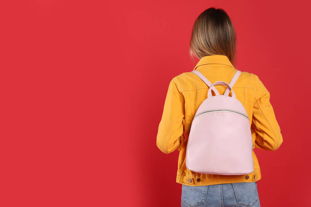 Woman with backpack on red background, back view. Space for text - Φωτογραφία, εικόνα