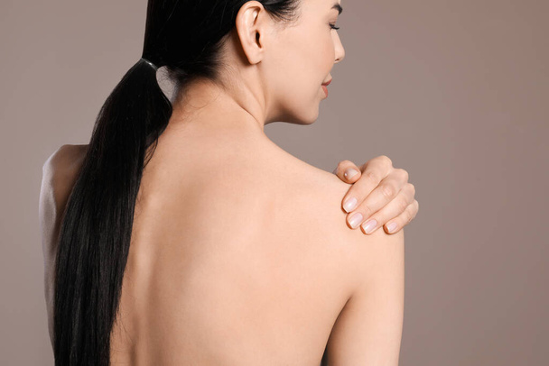 Woman suffering from shoulder pain on beige background, closeup - Foto, imagen