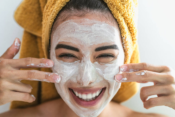 Jonge glimlachende vrouw die crème op het gezicht aanbrengt - Gelukkig meisje met huidverzorging spa dag thuis - Gezonde schoonheid schone behandeling en jeugd levensstijl concept - Foto, afbeelding