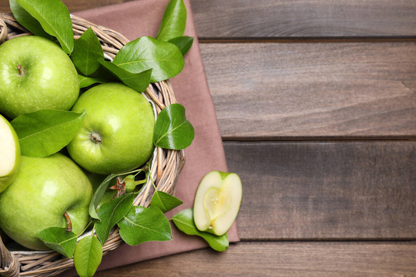 Manzanas verdes maduras frescas y hojas con canasta de mimbre sobre mesa de madera, puesta plana. Espacio para texto - Foto, Imagen