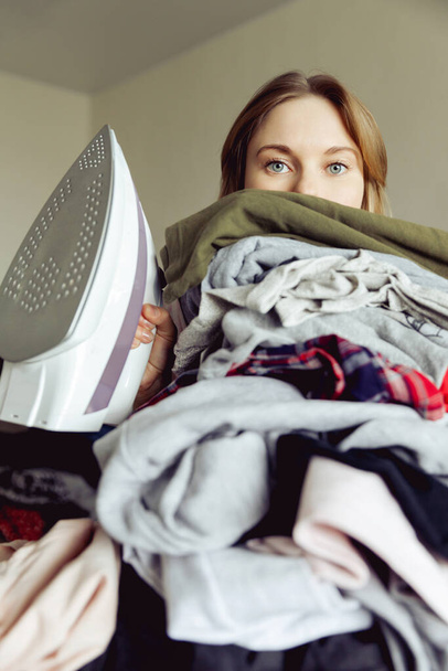 girl with an iron on the background of a large heap of clothes. before ironing - Фото, изображение