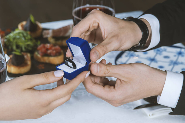 Мужские руки с синей бархатной коробкой, содержащей платежи смарт-кольцо. Мужчина дает женщине умное кольцо для платежей. Романтический ужин. День Святого Валентина - Фото, изображение