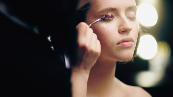 maquillaje borroso artista aplicando sombra de ojos líquido oscuro en el párpado del modelo  - Foto, imagen