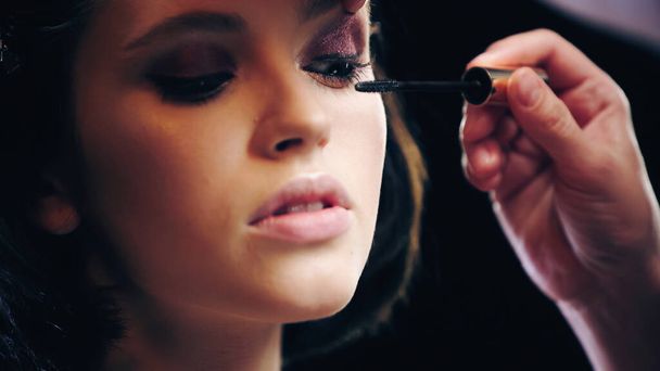 makeup artist applying black mascara on eyelashes of young woman - Photo, Image