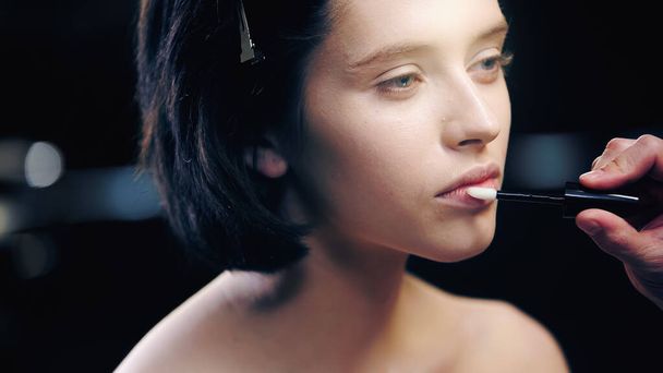 maquillador aplicando brillo labial sobre labios de modelo con hombros desnudos  - Foto, imagen