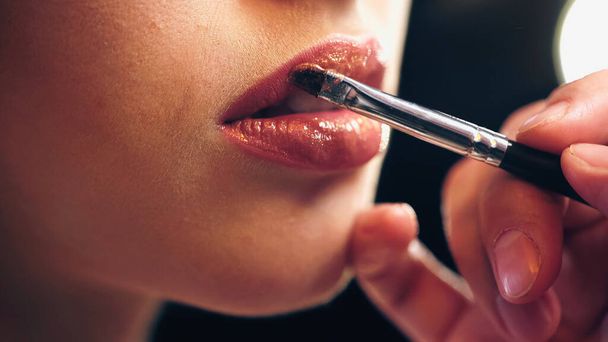 καλλιεργημένη άποψη του καλλιτέχνη μακιγιάζ εφαρμογή lip gloss στα χείλη της γυναίκας - Φωτογραφία, εικόνα