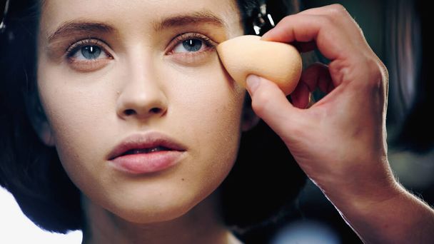 makeup artist εφαρμογή μακιγιάζ ίδρυμα με σφουγγάρι καλλυντικά στο δέρμα του όμορφου μοντέλου - Φωτογραφία, εικόνα