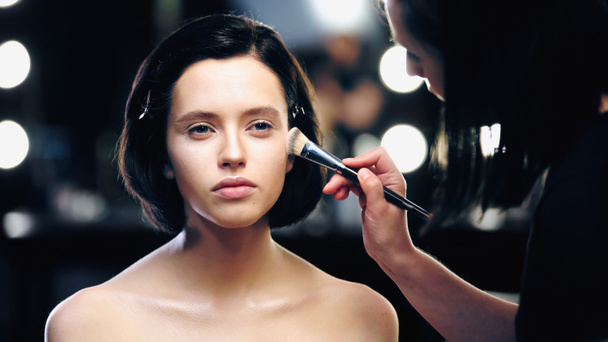 maquillaje artista aplicando maquillaje fundación con cepillo cosmético en la cara de morena modelo joven - Foto, imagen