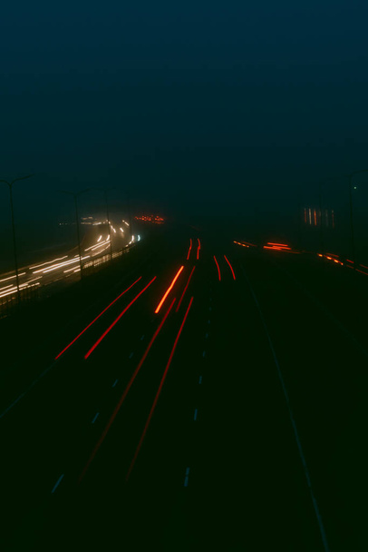 Zamazane światła na autostradzie w nocy. Mgła rośnie w tle. Bokeh, tło, humorzasty i filtr vintage - Zdjęcie, obraz