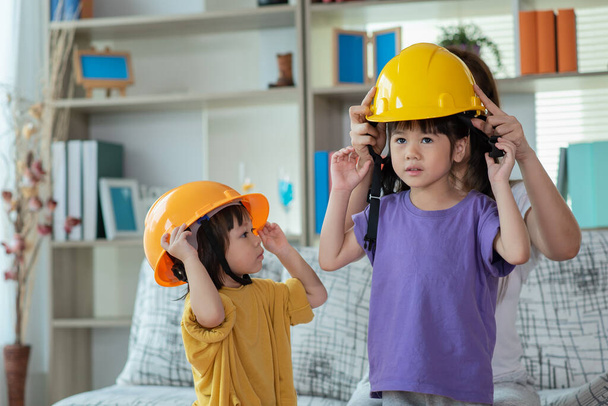 Asiática madre ayudar hija usando amarillo ingeniero casco, educación y ocupación concepto - Foto, imagen