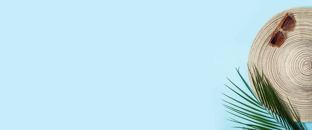 Sombrero de mujer con ala ancha, gafas de sol y una rama de una palmera sobre un fondo azul. Concepto de verano, vacaciones en el mar. Banner. Piso tendido, vista superior. - Foto, Imagen