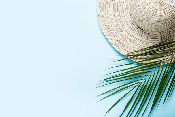 Women's hat with wide brim and a branch of a palm tree on a blue background. Summer concept, vacation at sea. Banner. Flat lay, top view. - Foto, Imagen