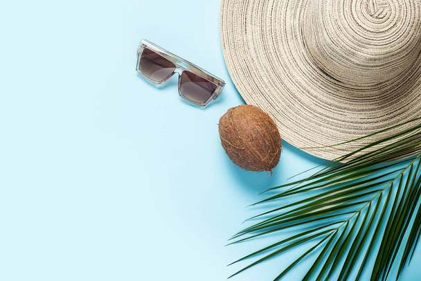 広いつば、サングラス、ココナッツと青い背景にヤシの木の枝を持つ女性の帽子。夏のコンセプト、海での休暇。バナーだ。フラットレイアウト、トップビュー. - 写真・画像