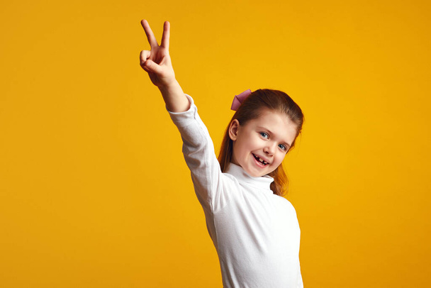 Симпатичный ребенок делает мирный жест с поднятой рукой на желтом фоне - Фото, изображение