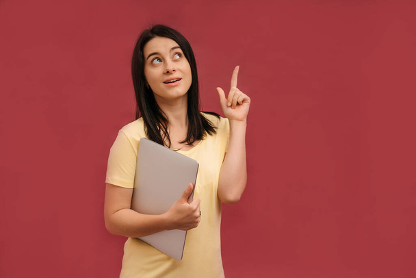 Imagen de una joven joven emocional optimista gritando sorprendida posando aislada sobre un fondo de pared rosa vestida con una camiseta casual amarilla usando una computadora portátil. - Foto, imagen