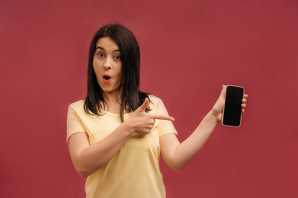 Изображение шокированной молодой красивой женщины, позирующей на фоне розовой стены, играющей в игры с помощью мобильного телефона. - Фото, изображение