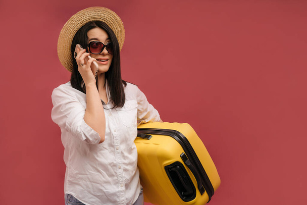 Side view traveler tourist woman in summer clothes hat hold yellow valise suitcase luggage isolated on pastel pink background. Passenger traveling abroad on weekends getaway Air flight journey concept - Photo, Image