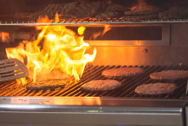 Hamburgers are charbroiled on a grill as flames shoot up through the grill grates.  - Photo, Image