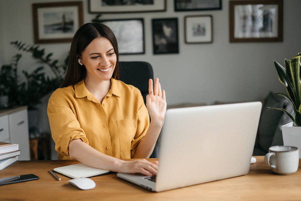 Genç esmer kadın evde çalışırken çevrimiçi toplantı için dizüstü bilgisayar kullanıyor. Video çağrısı - Fotoğraf, Görsel
