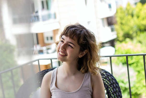 Young pretty curly girl smiling on balcony of apartment - Zdjęcie, obraz