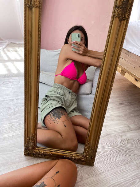 Fit gebräunte Frau mit perfektem Körper, Bauch, in Shorts und Bikini, Foto-Selfie mit dem Handy im Spiegel zu Hause für soziale Medien, Geschichten, senkrecht - Foto, Bild